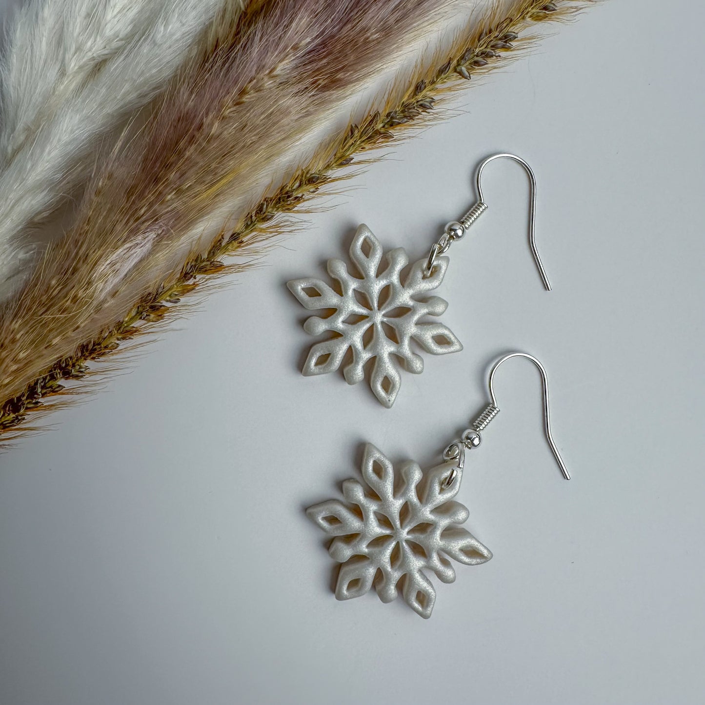 Handmade white polymer clay snowflake earrings with silver hooks by Purely Clayful.