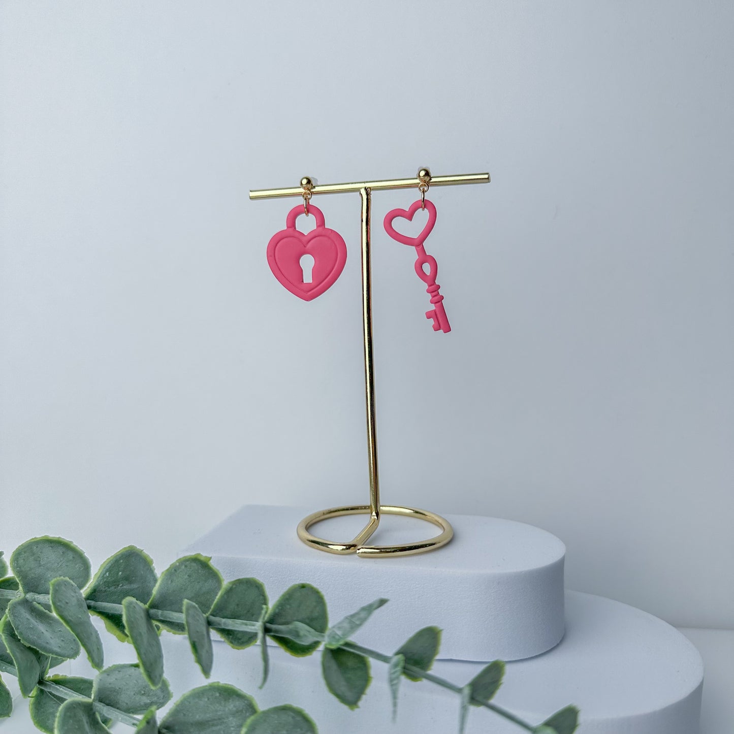 Handcrafted pink heart lock key earrings by Purely Clayful on a gold display stand.