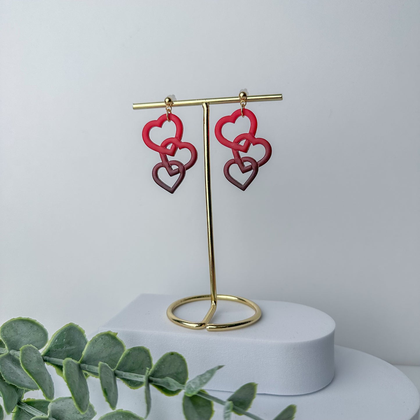 Interlocking red and purple heart dangle earrings by Purely Clayful on a gold display stand.