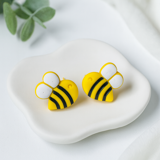 Bee-shaped earrings on a white dish with a light background