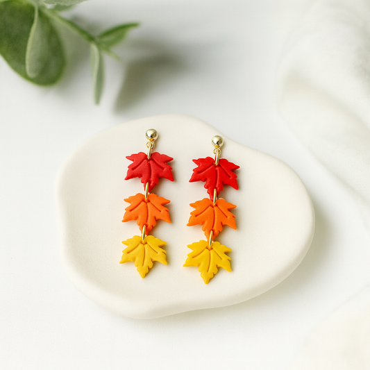 Colorful leaf-shaped earrings on a white stone with green leaves in the background