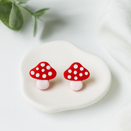 Mushroom-shaped earrings on a white stone with green leaves in the background