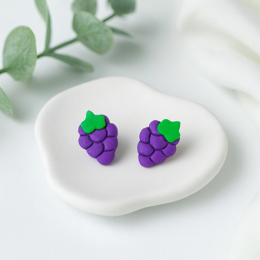 Purple grape-shaped earrings with green leaves on a white stone with a light background
