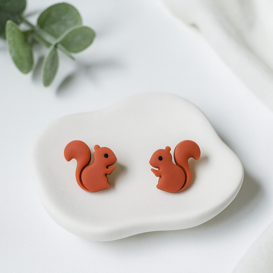 Red squirrel-shaped earrings on a white stone with a blurred green leaf background