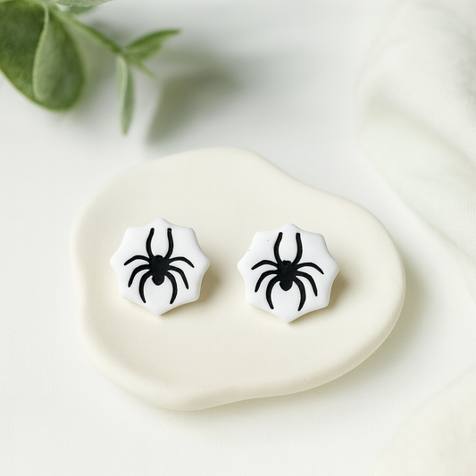 Spider earrings on a white stone with green leaves in the background
