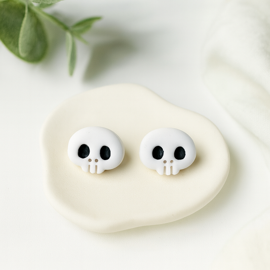 White skull-shaped earrings on a white stone with green leaves in the background